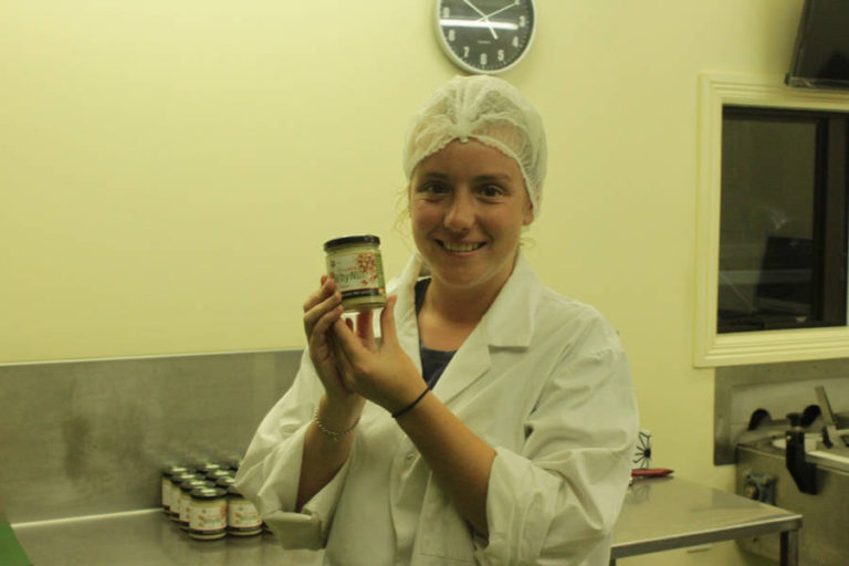 young girl wearing hair net and white coat holding jar of macadamia nut spread